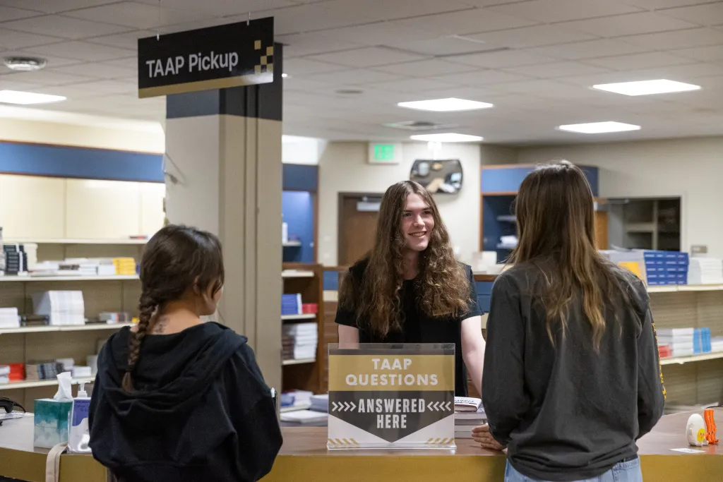 student working in the campus store talking to two other students about TAAP
